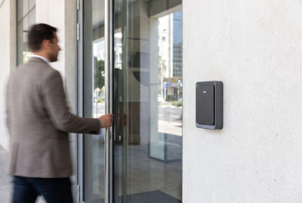 Biometric access control reader beside a glass office door as a person approaches
